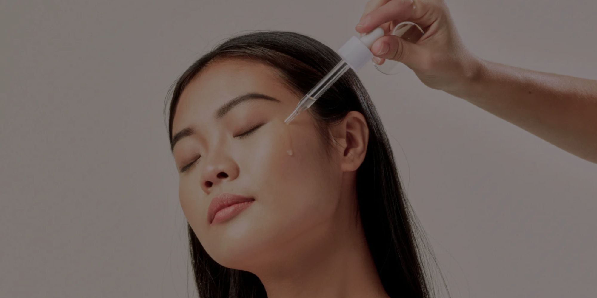 Person applying a product to a woman's face using a brush against a neutral background
