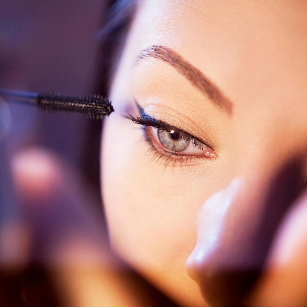 Person applying mascara to their eyelashes with a close-up focus on the eye.