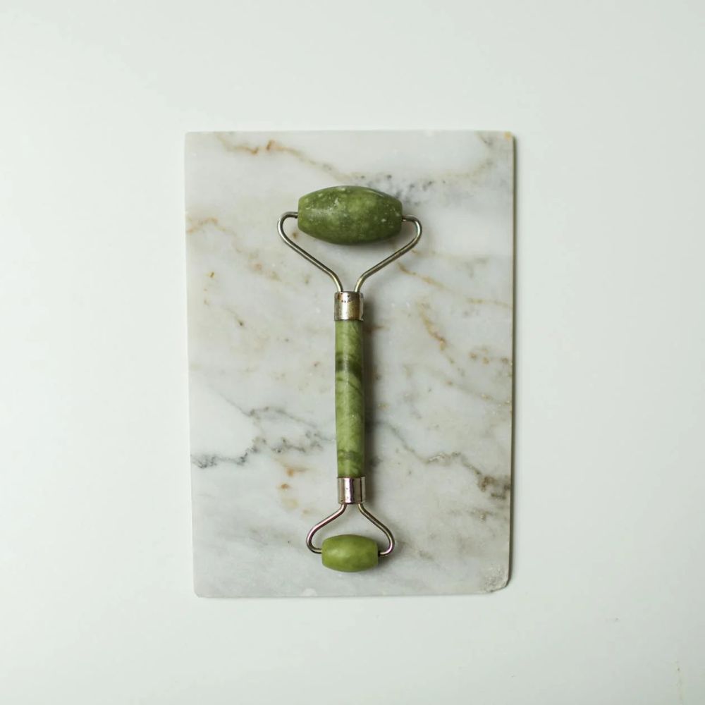 Green facial roller on a marble surface with a white background