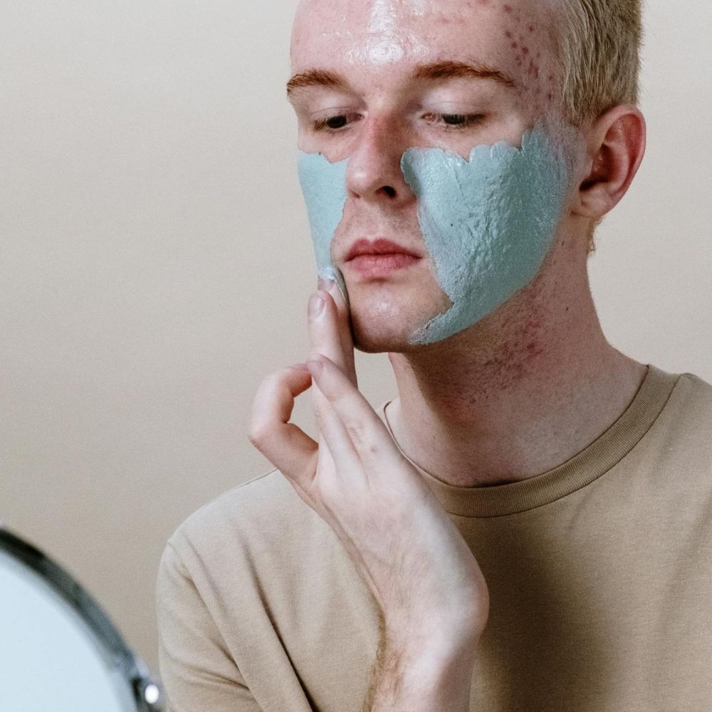 Man applying a face mask to his face with a neutral background

