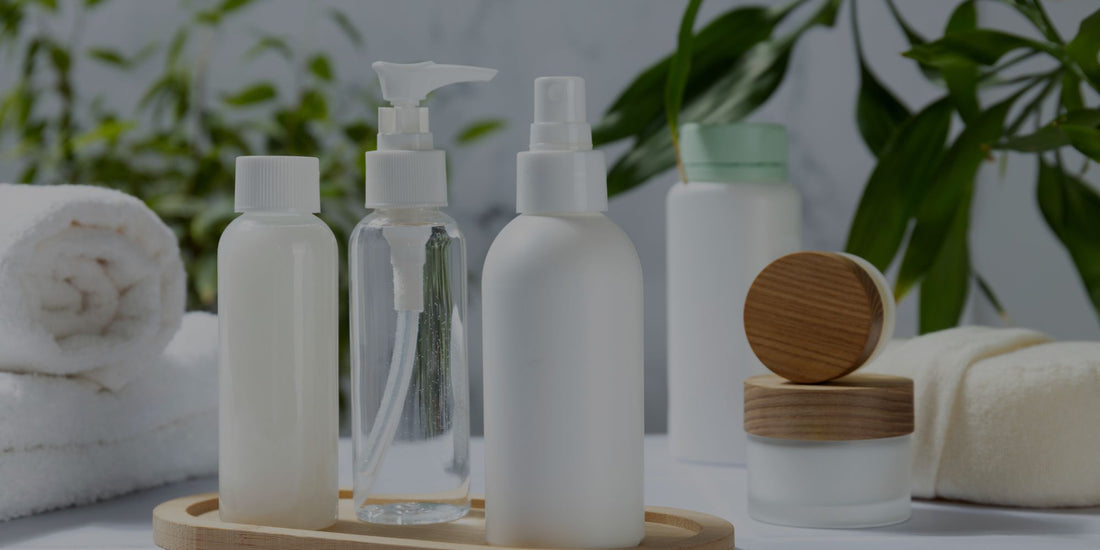 Set of skincare products including bottles and jars on a wooden tray with a blurred green plant background.